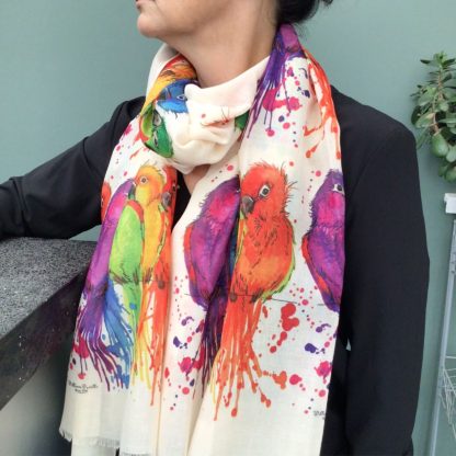 Blonde lady standing outside white buildings in chelsea, wearing an all back outfit, taupe jumper and a hand printed colourful parrots design scarf with black sunglasses on