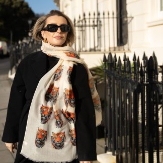 Blonde lady standing outside white buildings in chelsea, wearing an all back outfit, taupe jumper and a hand printed tiger head design scarf with black sunglasses on