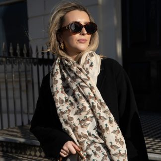 Blonde lady standing outside white buildings in chelsea, wearing an all back outfit, taupe jumper and a hand printed ducks design scarf with black sunglasses on holding tan leather bag