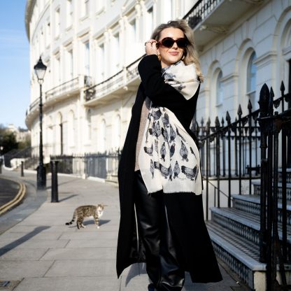 Blonde lady standing outside white buildings in chelsea, wearing an all back outfit and a hand printed chickens design scarf with black sunglasses on