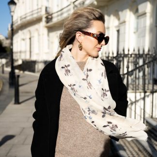 Blonde lady standing outside white buildings in chelsea, wearing an all back outfit, taupe jumper and a hand printed cows design scarf with black sunglasses on