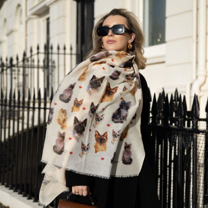 Blonde lady standing outside white buildings in chelsea holding a dark tan leather bag and wearing a hand printed cats and hearts scarf with sunglasses on