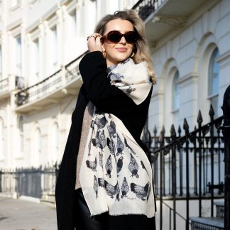 Blonde lady standing outside white buildings in chelsea, wearing an all back outfit, taupe jumper and a hand printed chickens design scarf with black sunglasses on