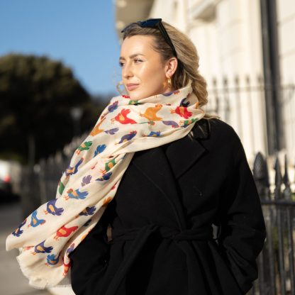 Blonde lady standing outside white buildings in chelsea, wearing an all back outfit, taupe jumper and a hand printed colourful Chickens design scarf with black sunglasses on