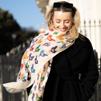 Blonde lady standing outside white buildings in chelsea, wearing an all back outfit, taupe jumper and a hand printed colourful Chickens design scarf with black sunglasses on