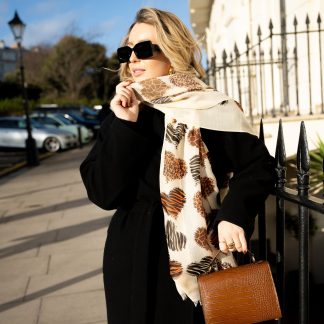 Blonde lady standing outside white buildings in chelsea holding a dark tan leather bag and wearing a hand printed animal print heart scarf with sunglasses on