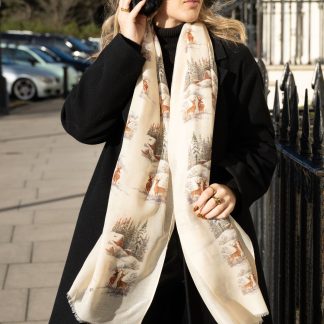 Blonde lady standing outside white buildings in chelsea, wearing an all back outfit, taupe jumper and a hand printed christmas scene design scarf with black sunglasses on