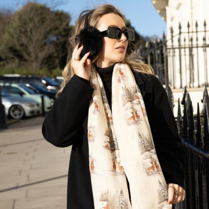 Blonde lady standing outside white buildings in chelsea, wearing an all back outfit, taupe jumper and a hand printed christmas scene design scarf with black sunglasses on