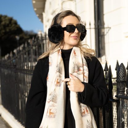 Blonde lady standing outside white buildings in chelsea, wearing an all back outfit, taupe jumper and a hand printed christmas scene design scarf with black sunglasses on