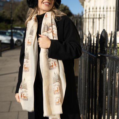 Blonde lady standing outside white buildings in chelsea, wearing an all back outfit, taupe jumper and a hand printed christmas scene design scarf with black sunglasses on