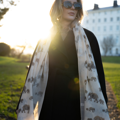 Blonde lady standing outside white buildings in chelsea, wearing an all back outfit, taupe jumper and a hand printed elephants design scarf with black sunglasses on