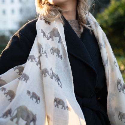 Blonde lady standing outside white buildings in chelsea, wearing an all back outfit, taupe jumper and a hand printed elephants design scarf with black sunglasses on