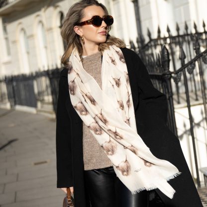 Blonde lady standing outside white buildings in chelsea, wearing an all back outfit, taupe jumper and a hand printed highland Cow design scarf with black sunglasses on