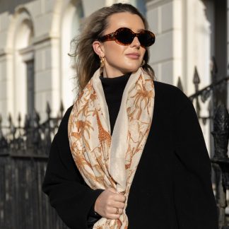 Blonde lady standing outside white buildings in chelsea, wearing an all back outfit, taupe jumper and a hand printed jungle animals design scarf with black sunglasses on