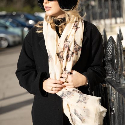 Blonde lady standing outside white buildings in chelsea, wearing an all back outfit, taupe jumper and a hand printed pigs design scarf with black sunglasses on