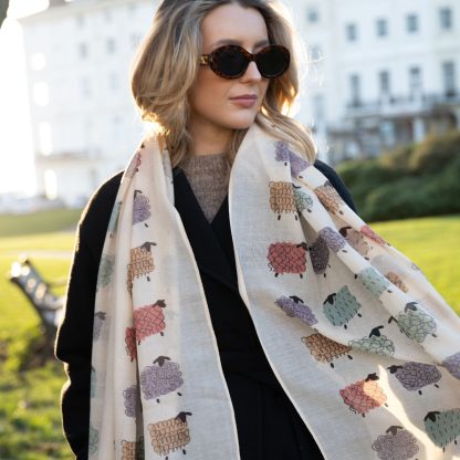 outside white buildings in chelsea, wearing an all back outfit, taupe jumper and a hand printed colourful sheep design scarf with black sunglasses on