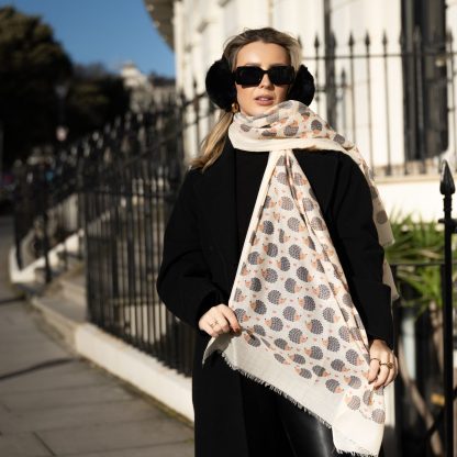 Blonde lady standing outside white buildings in chelsea, wearing an all back outfit, taupe jumper and a hand printed hedgehogs design scarf with black sunglasses on