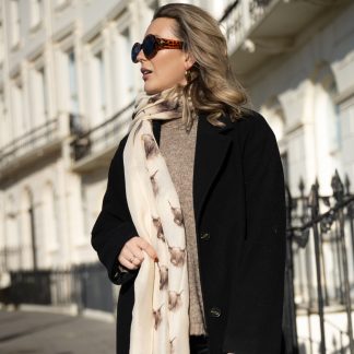 Blonde lady standing outside white buildings in chelsea, wearing an all back outfit, taupe jumper and a hand printed highland Cow design scarf with black sunglasses on