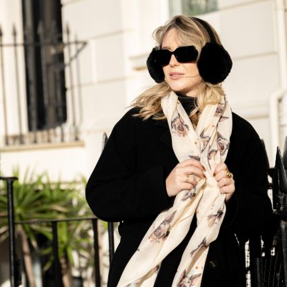 Blonde lady standing outside white buildings in chelsea, wearing an all back outfit, taupe jumper and a hand printed pigs design scarf with black sunglasses on