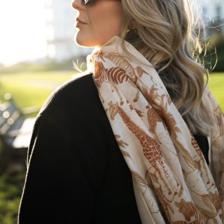 Blonde lady standing outside white buildings in chelsea, wearing an all back outfit, taupe jumper and a hand printed jungle animals design scarf with black sunglasses on