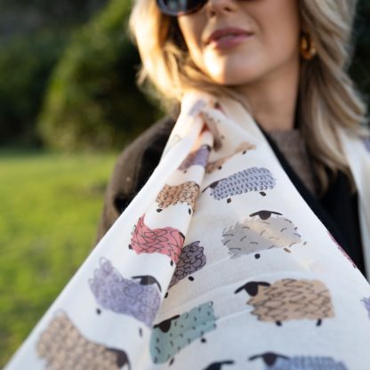 outside white buildings in chelsea, wearing an all back outfit, taupe jumper and a hand printed colourful sheep design scarf with black sunglasses on