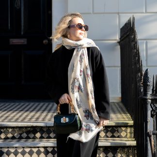 Blonde lady standing outside white buildings in chelsea, wearing an all back outfit, taupe jumper and a hand printed funky zebra wearing pink glasses design scarf with black sunglasses on