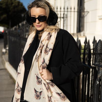 Blonde lady standing outside white buildings in chelsea, wearing an all back outfit, taupe jumper and a hand printed pigs design scarf with black sunglasses on