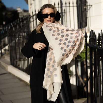 Blonde lady standing outside white buildings in chelsea, wearing an all back outfit, taupe jumper and a hand printed hedgehogs design scarf with black sunglasses on