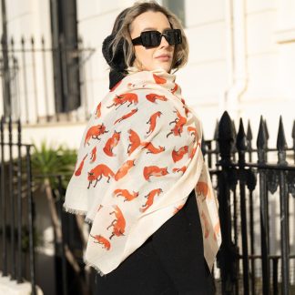 Blonde lady standing outside white buildings in chelsea, wearing an all back outfit, taupe jumper and a hand printed foxes design scarf with black sunglasses on