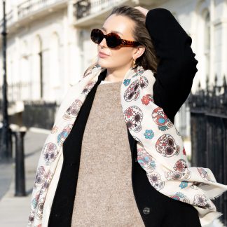 Blonde lady standing outside white buildings in chelsea, wearing an all back outfit, taupe jumper and a hand printed sugar skulls design scarf with black sunglasses on