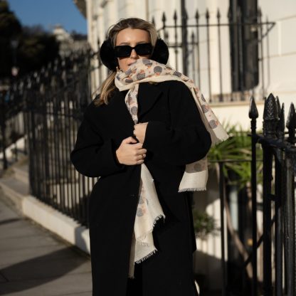 Blonde lady standing outside white buildings in chelsea, wearing an all back outfit, taupe jumper and a hand printed hedgehogs design scarf with black sunglasses on