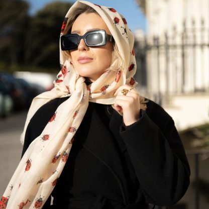 Blonde lady standing outside white buildings in chelsea, wearing an all back outfit, taupe jumper and a hand printed ladybird design scarf with black sunglasses on