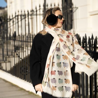 outside white buildings in chelsea, wearing an all back outfit, taupe jumper and a hand printed colourful sheep design scarf with black sunglasses on