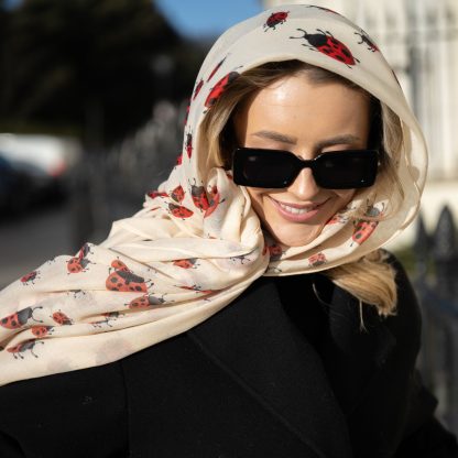 Blonde lady standing outside white buildings in chelsea, wearing an all back outfit, taupe jumper and a hand printed ladybird design scarf with black sunglasses on