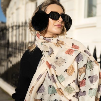 outside white buildings in chelsea, wearing an all back outfit, taupe jumper and a hand printed colourful sheep design scarf with black sunglasses on