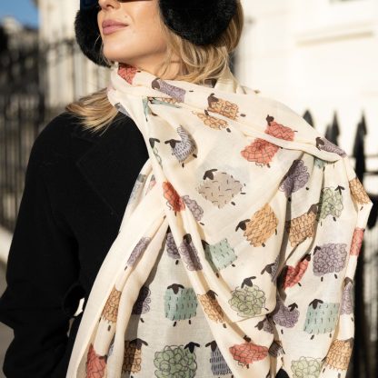 outside white buildings in chelsea, wearing an all back outfit, taupe jumper and a hand printed colourful sheep design scarf with black sunglasses on