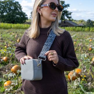 Blonde female model wearing a beautiful crossbody bag strap printed with a gothic lace design in a pumpkin field