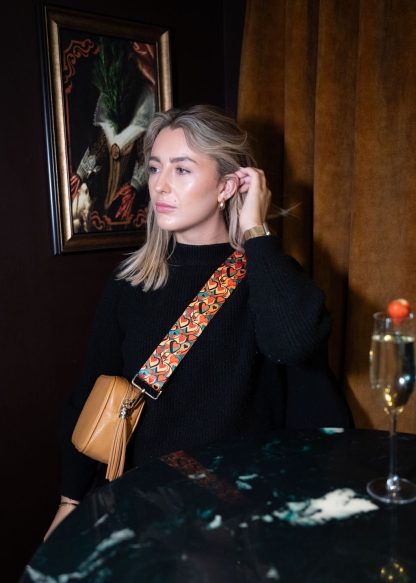 Blonde female model wearing a beautiful crossbody bag strap printed with a retro heart design in a cocktail bar