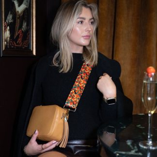 Blonde female model wearing a beautiful crossbody bag strap printed with a retro heart design in a cocktail bar