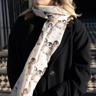 Blonde lady standing outside white buildings in chelsea, wearing an all back outfit, taupe jumper and a hand printed christmas cute penguins design scarf with black sunglasses on