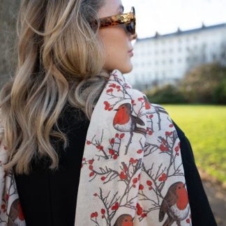 Blonde lady standing outside white buildings in chelsea, wearing an all back outfit, taupe jumper and a hand printed christmas Robins design scarf with black sunglasses on