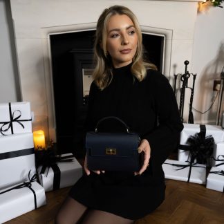 Blonde lady holding Black genuine italian leather crossbody bag in front of a fireplace, a gift for her this christmas, wearing all black with black and white presents