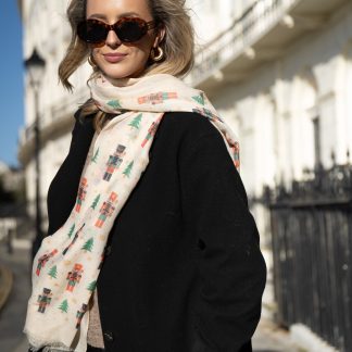 Blonde lady standing outside white buildings in chelsea, wearing an all back outfit, taupe jumper and a hand printed christmas Nutcrackers design scarf with black