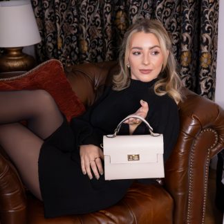 Blonde lady holding Cream genuine italian leather crossbody bag in front of a fireplace, a gift for her this christmas, wearing all black with black and white presents