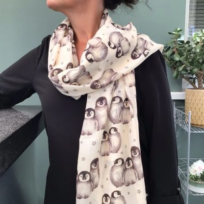 Cream coloured scarf being worn over one shoulder printed with a cute penguin design all over