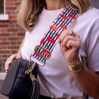 Blonde women wearing cherry bag strap on an italian leather crossbody navy bag, white tshirt, gold jewellery and watch