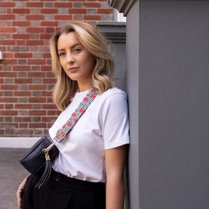 Blonde women wearing cherry bag strap on an italian leather crossbody navy bag, white tshirt, gold jewellery and watch