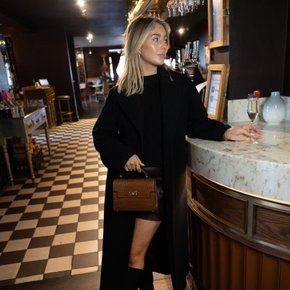 Blonde lady holding tan genuine italian leather croc crossbody bag, standing at a bar in chelsea in black outfit , holding a glass of champagne