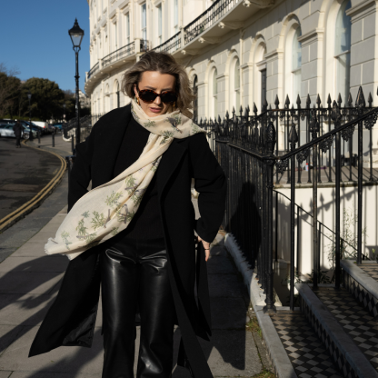 Blonde lady standing outside white buildings in chelsea, wearing an all back outfit, taupe jumper and a hand printed finch birds design scarf with black sunglasses on