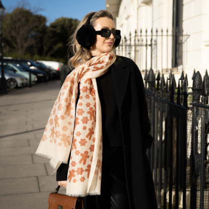 Blonde lady standing outside white buildings in chelsea, wearing an all back outfit, taupe jumper and a hand printed gingerbread man design scarf with black sunglasses on holing a tan italian leather crossbody bag